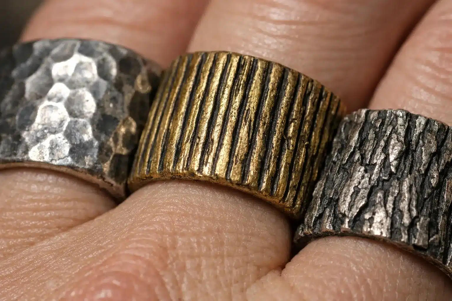 Close-up detail of brutalist jewelry surface textures including hammered, reeded, and bark finishes_risultato
